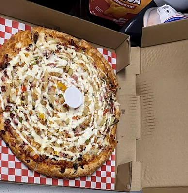 Pizza with a creamy sauce swirl in an open box on a red-checked liner