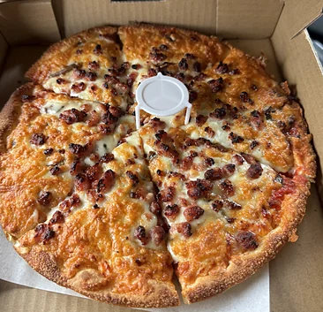 Bacon pizza cut into slices in an open takeout box