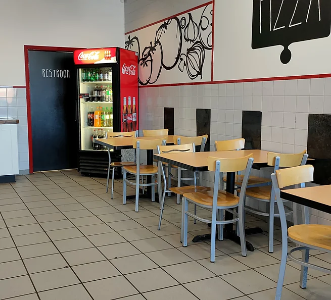 Dining room at Nitza's Pizza with tables, chairs and a drinks cooler